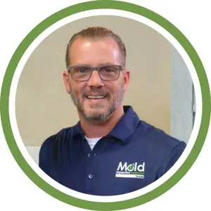 Smiling man with glasses and short hair, wearing a navy blue Mold Inspection Sciences polo shirt, stands in front of a beige wall. The image is framed by a green and white circular border, highlighting his expertise in inspection and assessment.
