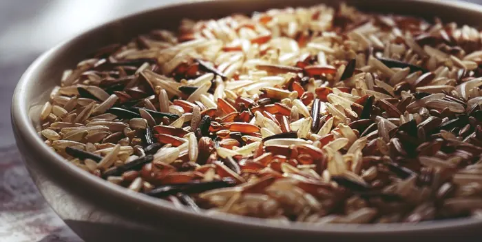 A close-up of a bowl filled with mixed rice varieties shows a blend of white, red, and black grains, creating a colorful and textured surface. Upon closer inspection, the delightful contrast reveals an artful culinary tapestry against a soft, blurred background.